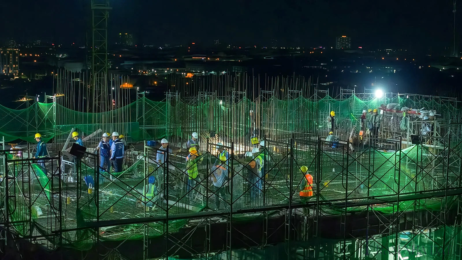 Nhóm kỹ sư xây dựng và giám sát công trường đứng kiểm tra bản vẽ và kết cấu tại sàn thi công một tòa tháp căn hộ, trang phục bảo hộ đầy đủ, bối cảnh công trường thật với cốt pha, thép, bê tông và cần cẩu phía sau